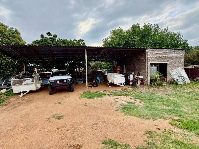An open-sided carport structure with a corrugated metal roof and brick masonry walls, providing basic covered parking space.