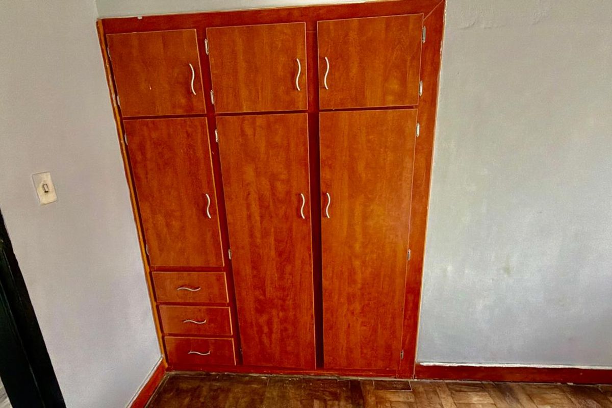 A bedroom featuring a large built-in wooden wardrobe and classic parquet flooring, offering a functional storage solution in a dated space.