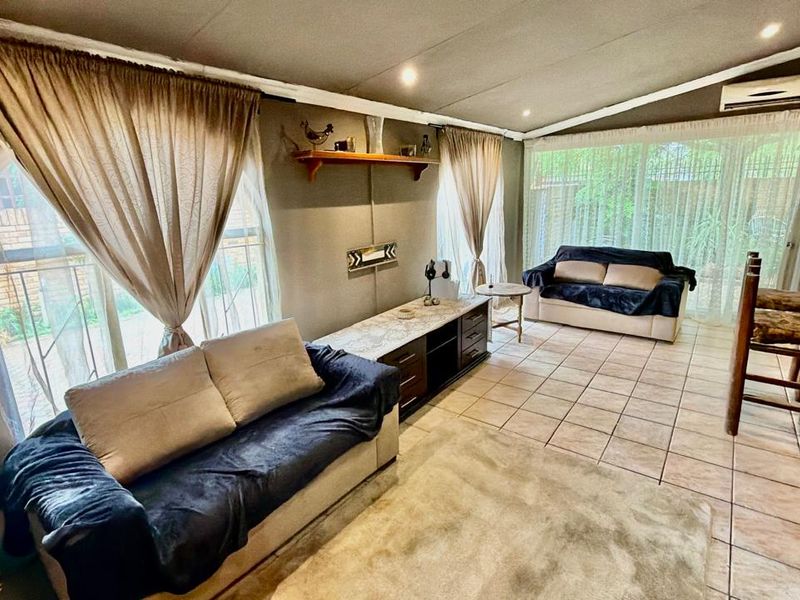 A spacious living area featuring tiled flooring, recessed lighting, and a wall-mounted air conditioning unit, with large windows providing natural light.