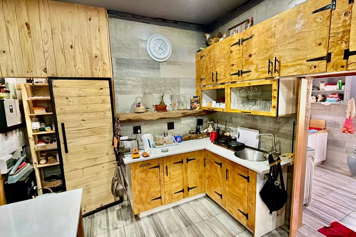 A rustic-style kitchen featuring custom wooden cabinetry, stone countertops, a stainless steel sink, and a floating shelf against a tiled feature wall.