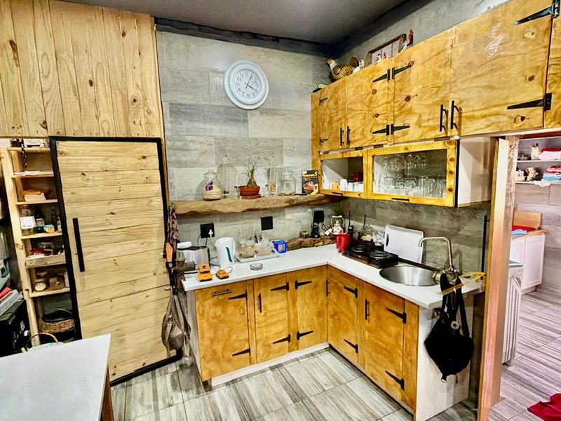 A rustic-style kitchen featuring custom wooden cabinetry, stone countertops, a stainless steel sink, and a floating shelf against a tiled feature wall.