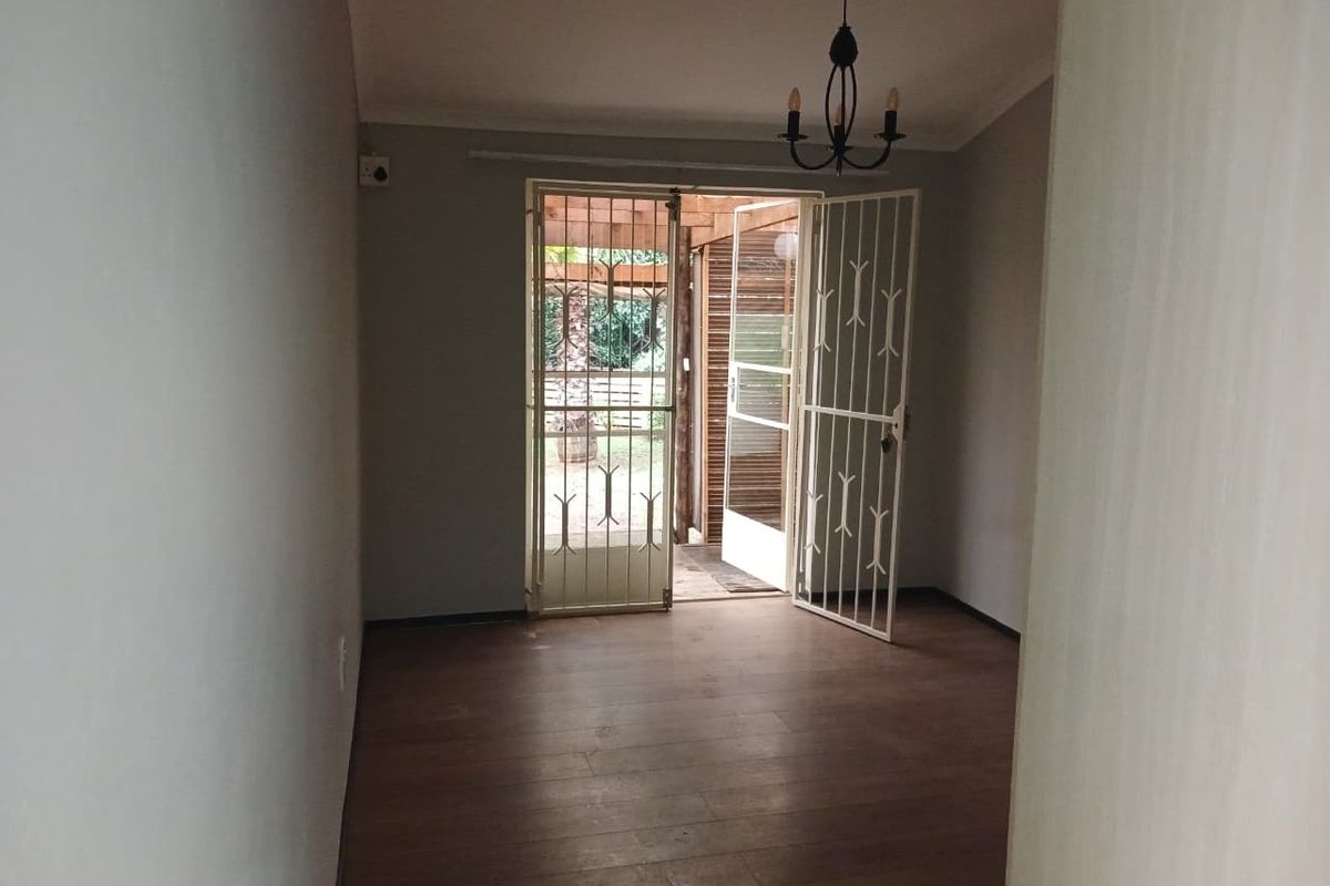 An empty living room featuring laminate flooring and a security gate providing direct access to an outdoor patio area.