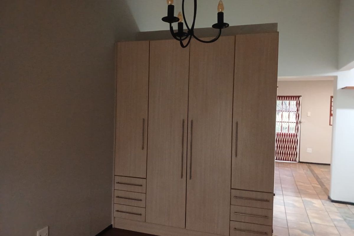 A bedroom featuring a large, light-wood built-in wardrobe with integrated drawers and a decorative ceiling light fixture.