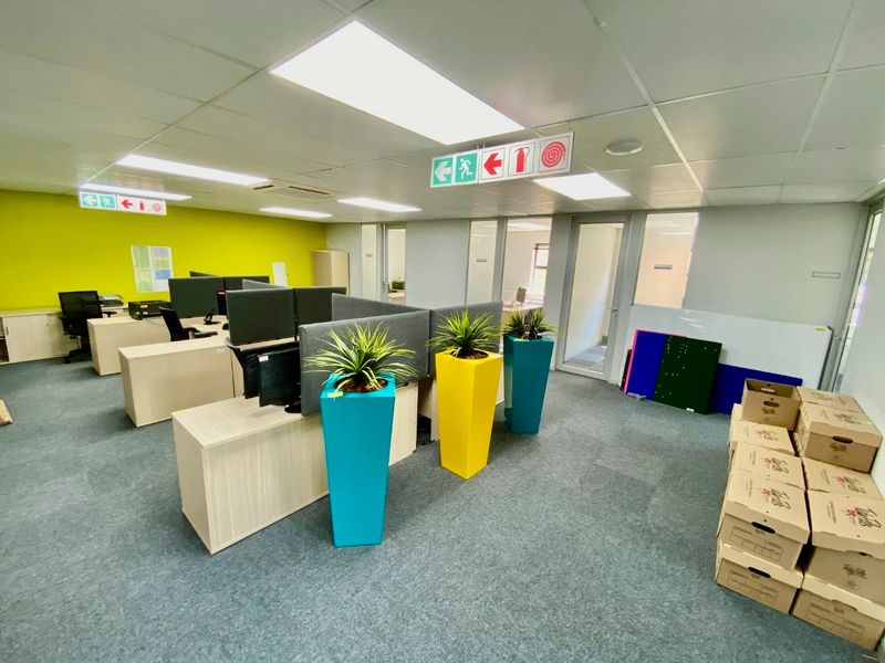A modern commercial office space featuring carpeted flooring, suspended ceilings with recessed lighting, and glass partition walls for a professional work environment.