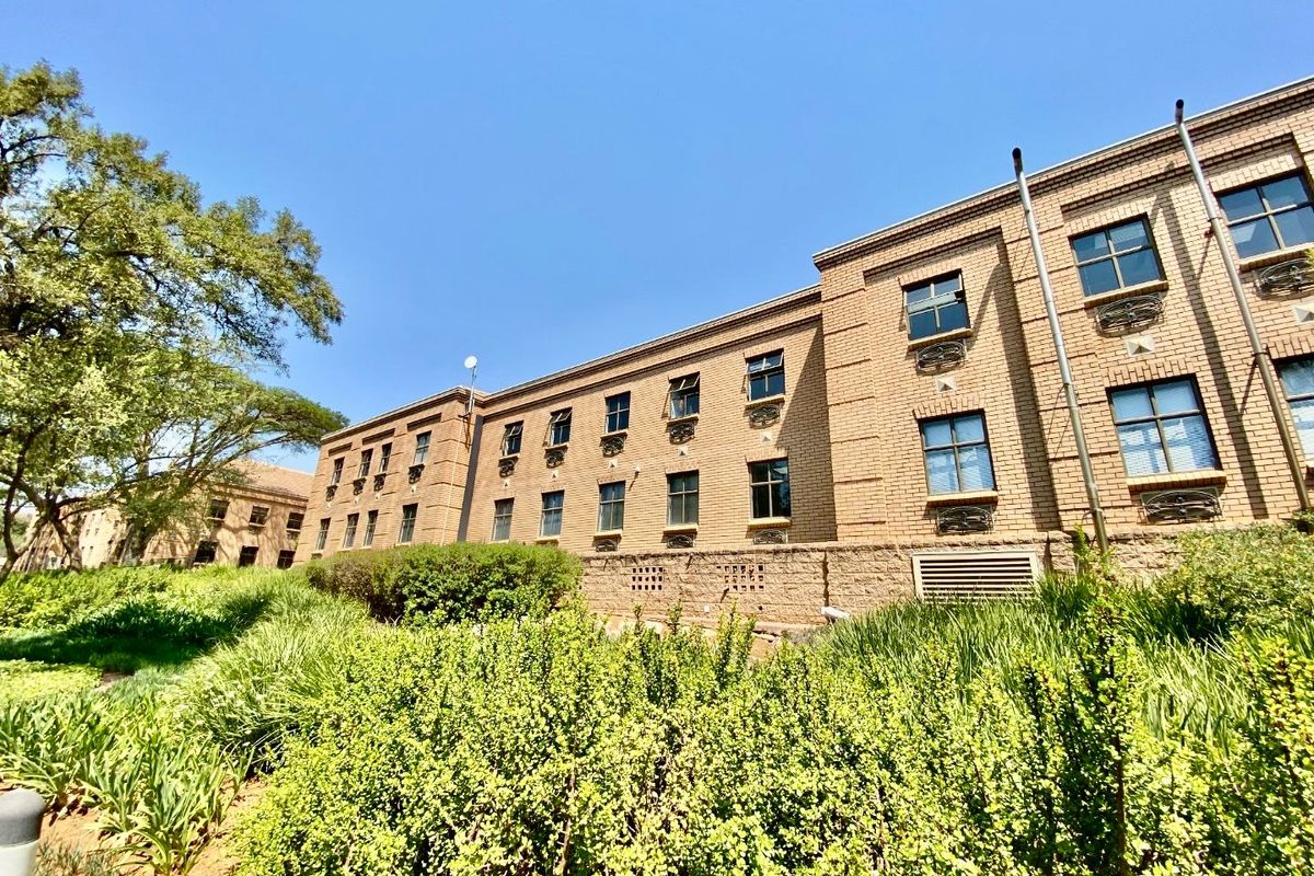 A view of the rear brick facade of the commercial building, featuring multiple windows and well-maintained surrounding garden landscaping.