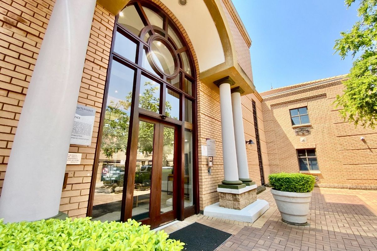 A well-maintained commercial building entrance featuring a prominent arched glass doorway, brick facade, and decorative columns leading into a paved courtyard area.