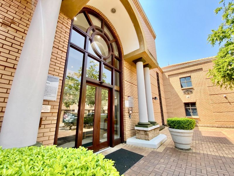 A well-maintained commercial building entrance featuring a prominent arched glass doorway, brick facade, and decorative columns leading into a paved courtyard area.
