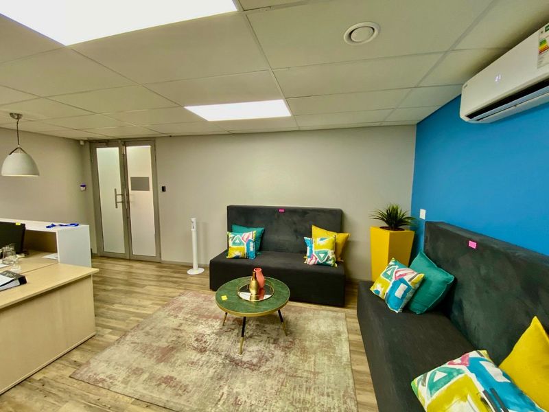 A modern commercial office space featuring laminate flooring, a suspended ceiling with recessed lighting, and a wall-mounted split-system air conditioning unit.
