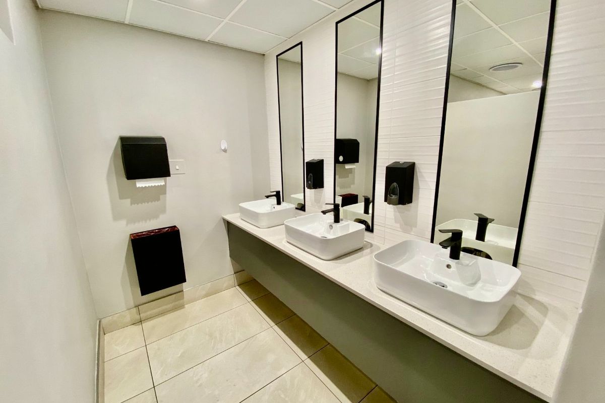 Modern commercial bathroom featuring a triple vanity with vessel sinks, wall-mounted faucets, large mirrors, and clean tiled finishes.