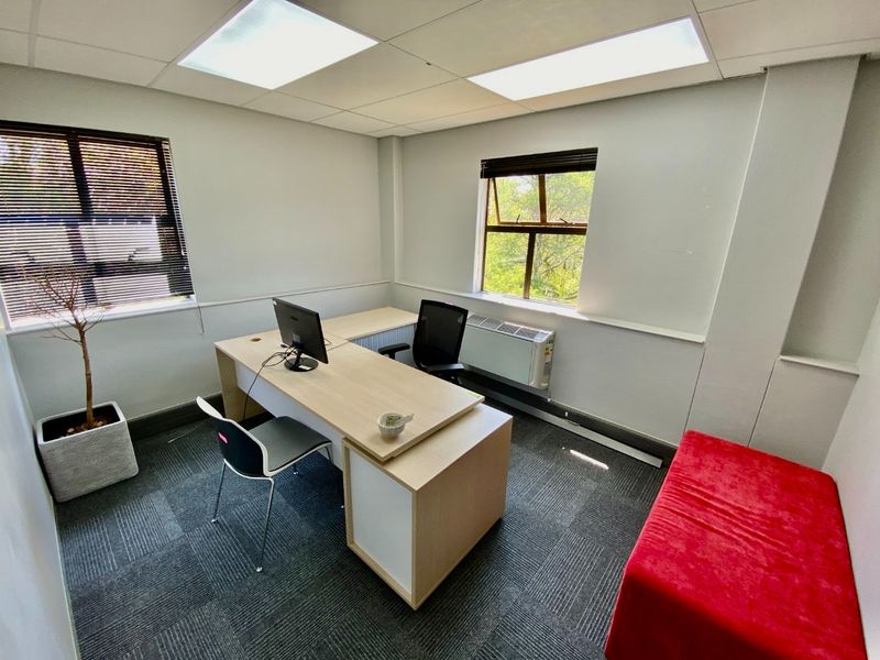A functional commercial office space featuring carpeted flooring, suspended ceiling with recessed lighting, and a wall-mounted heater.