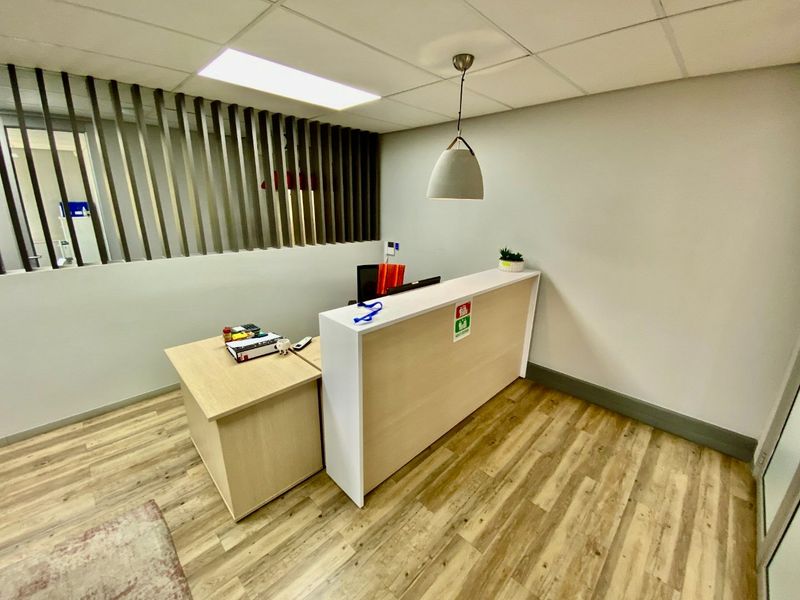 A modern commercial office reception area featuring a built-in desk, timber-look flooring, a decorative timber slat partition, and contemporary pendant lighting.
