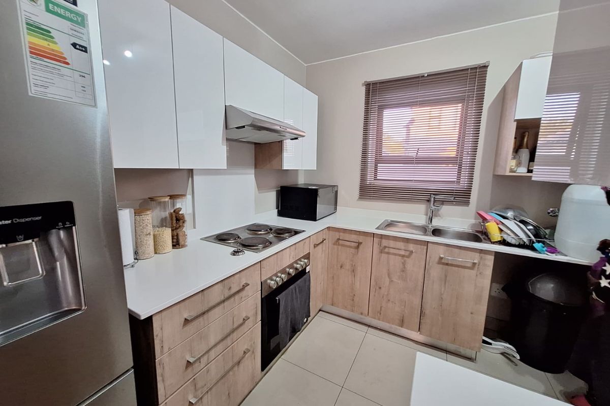 Modern kitchen featuring white gloss upper cabinets, wood-look lower cabinetry, electric hob, built-in oven, extractor fan, and a double sink with tiled flooring.