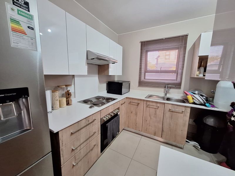 Modern kitchen featuring white gloss upper cabinets, wood-look lower cabinetry, electric hob, built-in oven, extractor fan, and a double sink with tiled flooring.