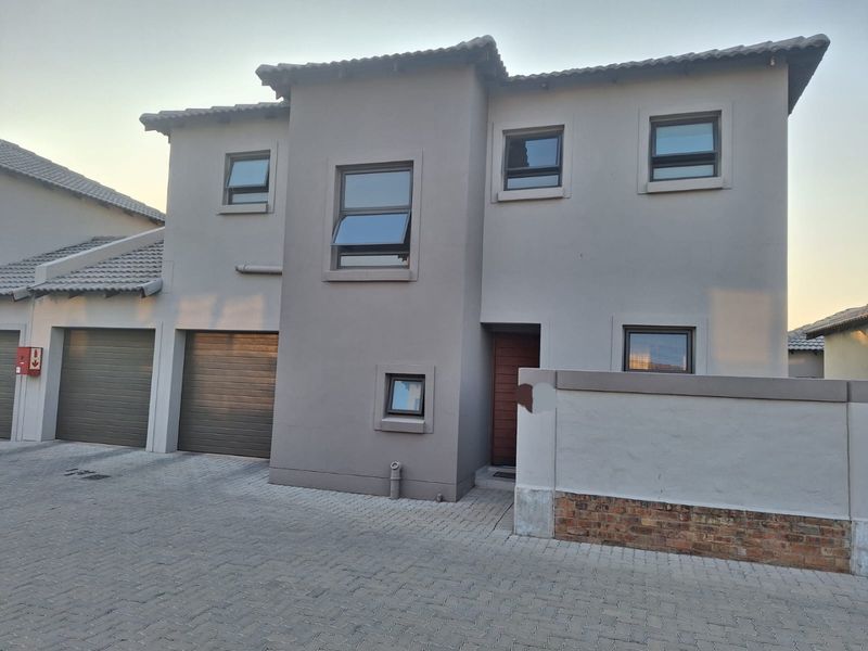Front elevation of a modern double-storey townhouse featuring a paved driveway, double garage, and neutral exterior finish.