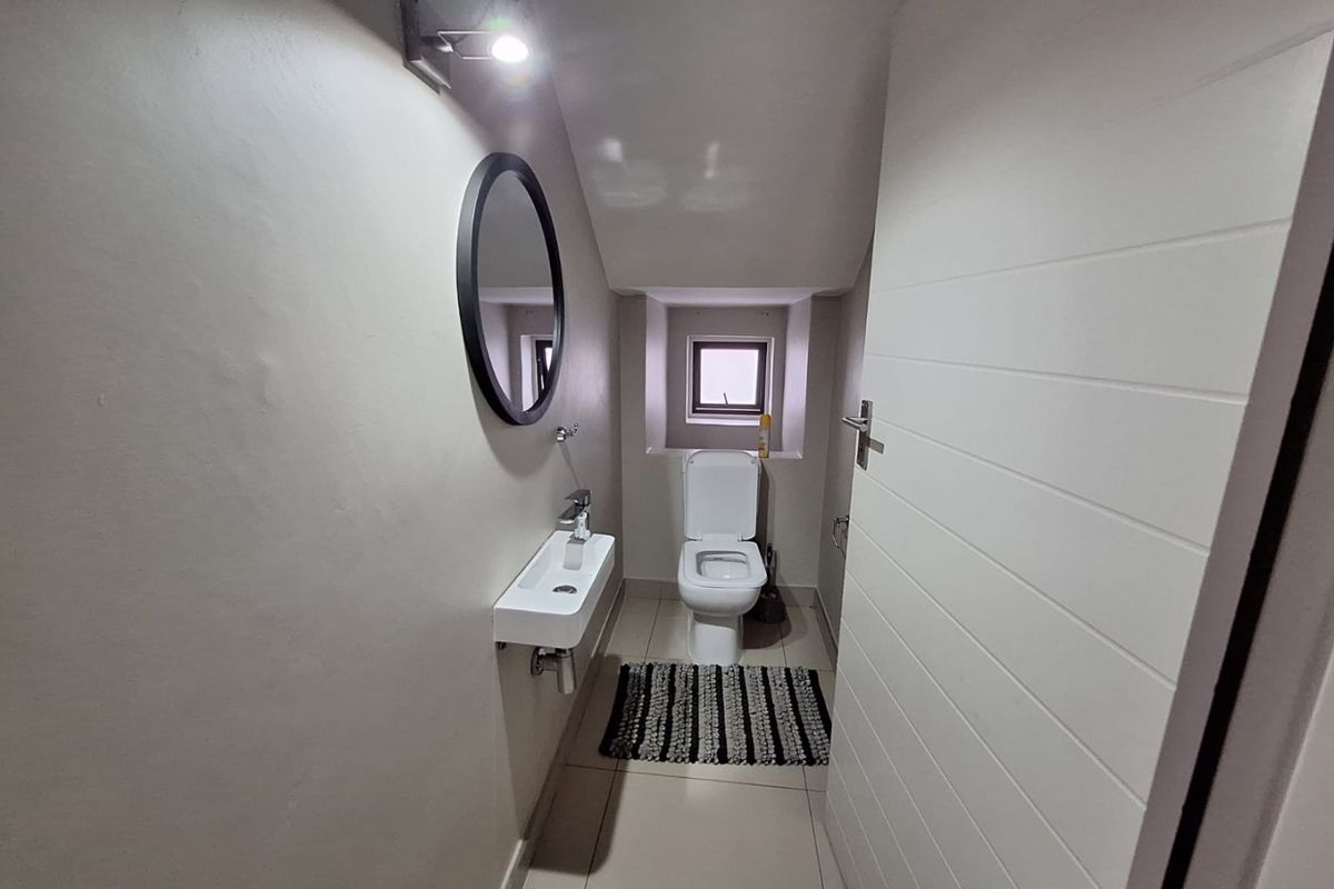 A compact guest bathroom featuring a wall-mounted basin, toilet, tiled flooring, and a small window, finished with neutral tones.