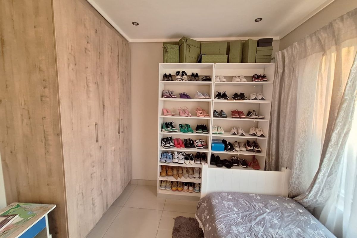A bedroom featuring light wood-finish built-in cupboards, tiled flooring, and recessed downlighting, providing ample storage and a neutral aesthetic.