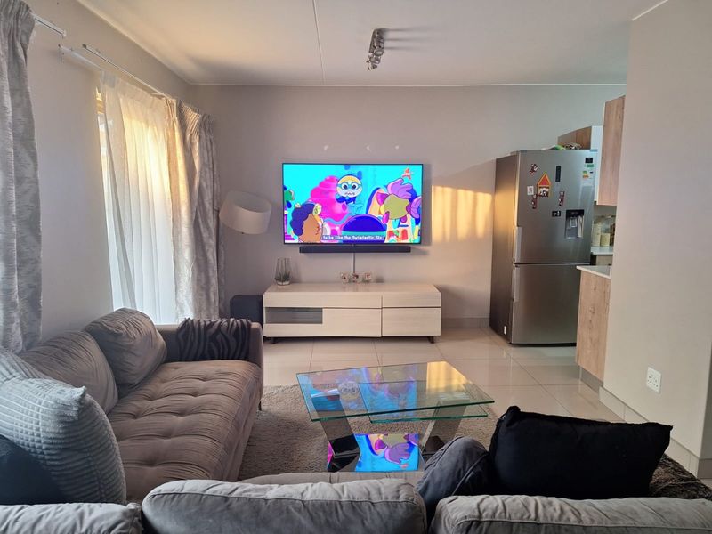 An open-plan living area featuring tiled flooring, integrated kitchen cabinetry, and a modern layout that seamlessly connects the lounge and kitchen spaces.