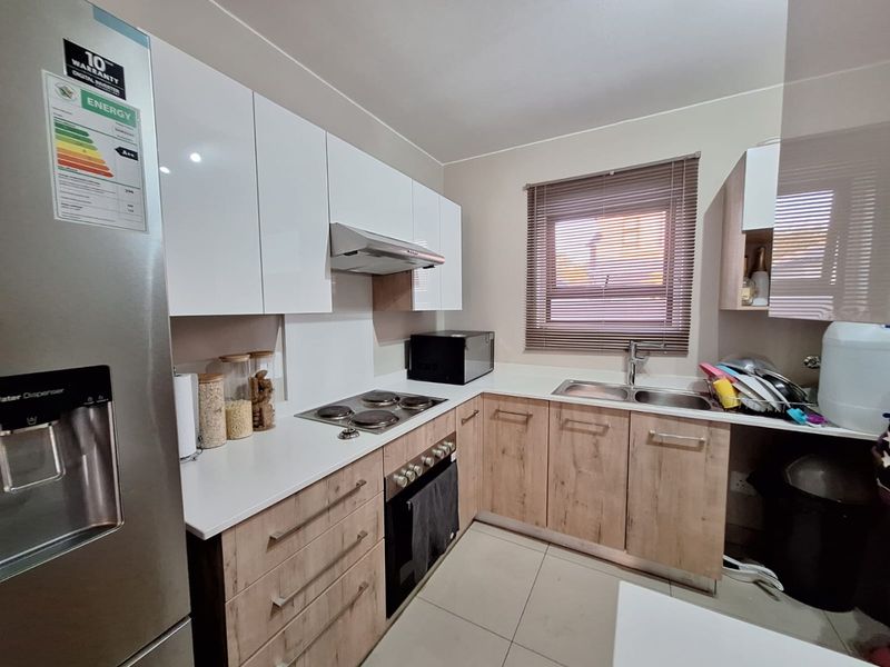 Modern kitchen featuring white gloss upper cabinets, wood-look lower cabinetry, electric hob, built-in oven, extractor fan, and a double sink with tiled flooring.
