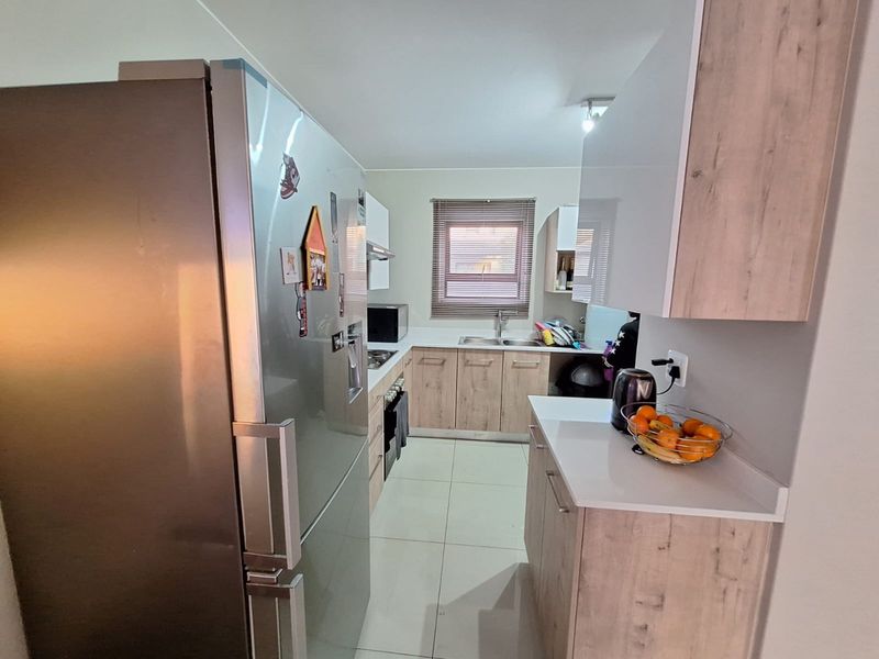 Modern kitchen featuring light wood-look cabinetry, stone-effect countertops, stainless steel sink, and integrated cooking appliances with tiled flooring.