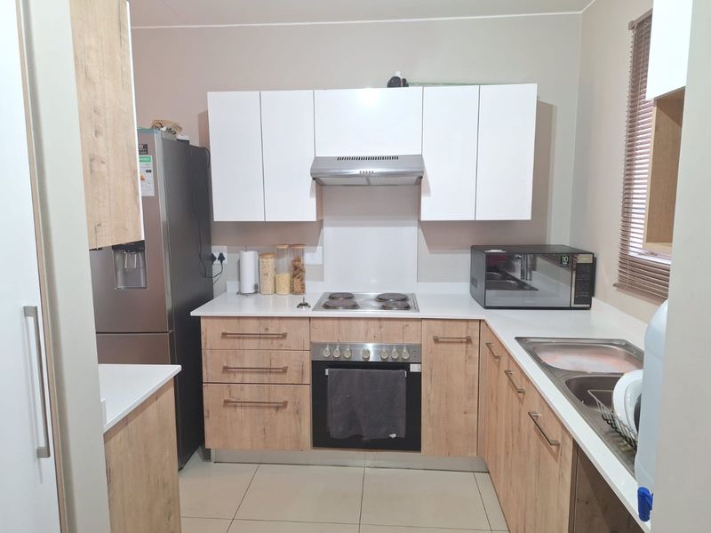 Modern kitchen featuring light wood-grain cabinetry, white stone countertops, built-in oven, electric hob, and stainless steel sink with tiled flooring.