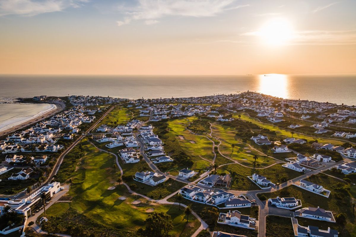 An elevated aerial view of a coastal residential estate featuring a golf course and proximity to the ocean at sunset.