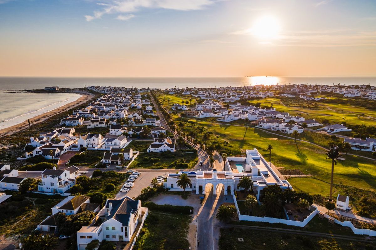 An aerial view of a coastal residential estate featuring a golf course, beach access, and a prominent gated entrance at sunset.