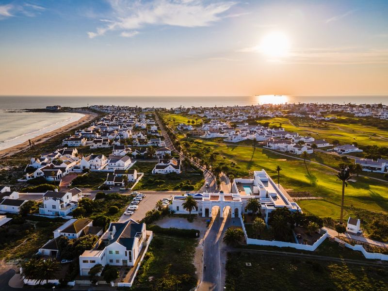 An aerial view of a coastal residential estate featuring a golf course, beach access, and a prominent gated entrance at sunset.