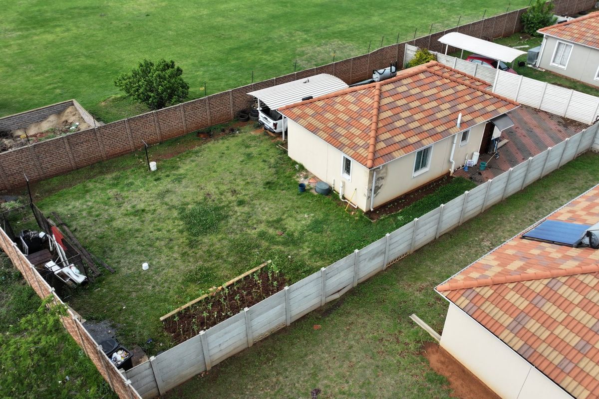 Aerial view of a residential property featuring a tiled roof house, private garden, paved driveway, carport, and perimeter boundary walling.