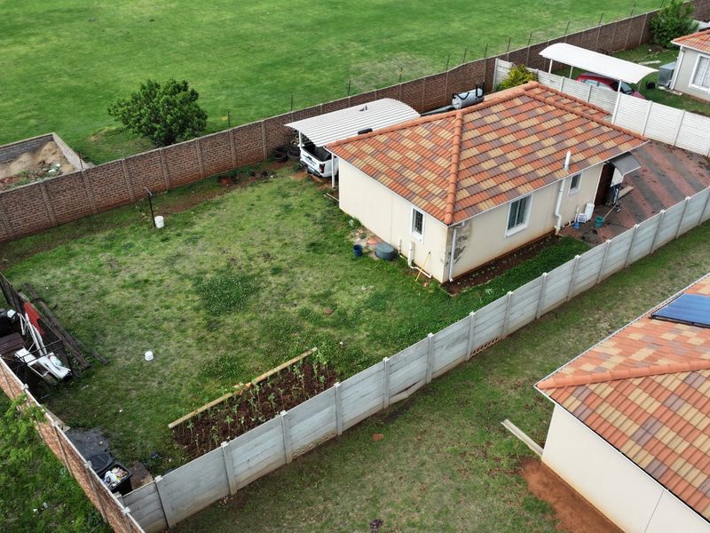 Aerial view of a residential property featuring a tiled roof house, private garden, paved driveway, carport, and perimeter boundary walling.