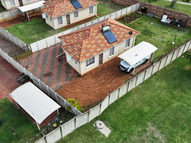 Aerial view of a residential property featuring a tiled roof with solar geyser, paved driveway, carport, and enclosed yard with precast boundary walls.