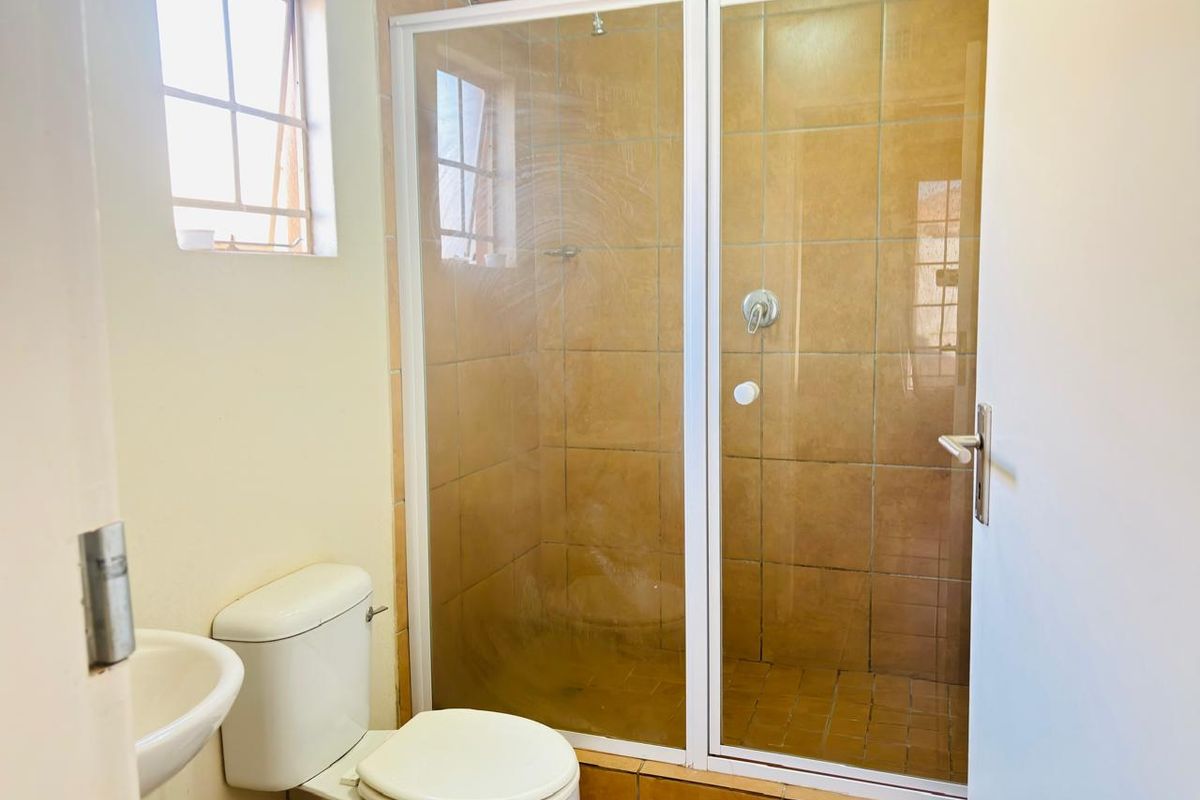 A functional bathroom featuring a shower enclosure with tiled walls, a standard toilet, and a wall-mounted basin.