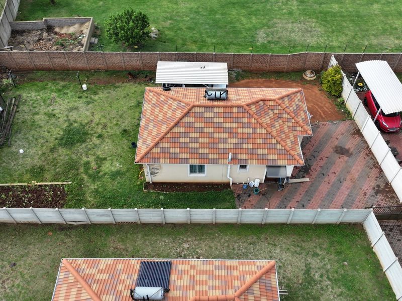 Aerial view of a residential property featuring a tiled roof with solar water heating, a paved driveway, carport, and enclosed garden space.