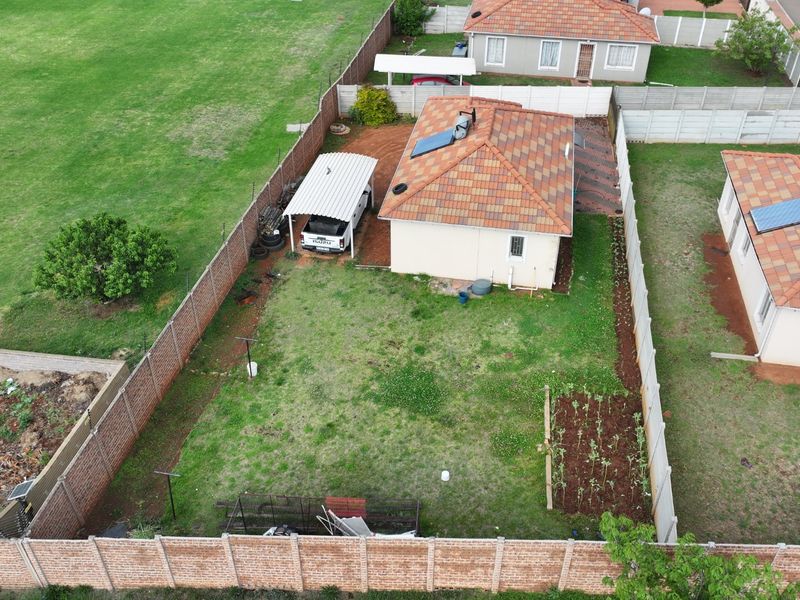 Aerial view of the property showing the house, tiled roof with solar geyser, carport, and enclosed backyard with boundary walls.