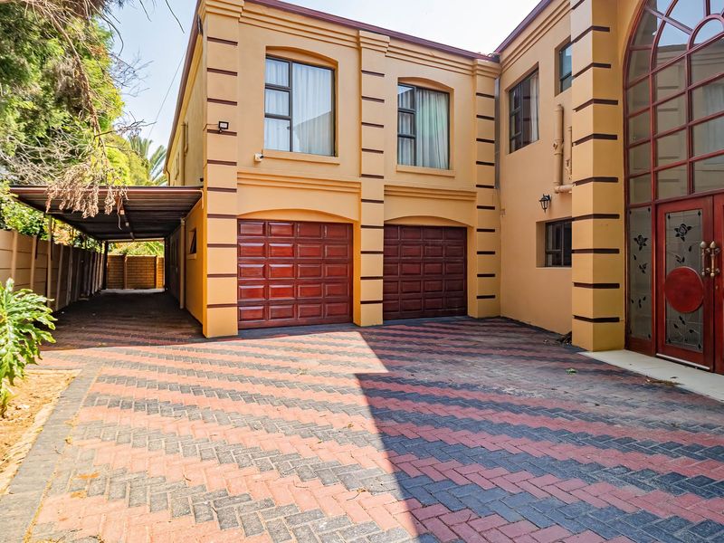 Front exterior view featuring a double garage, attached carport, paved driveway, and a prominent arched entrance door on a double-storey residence.