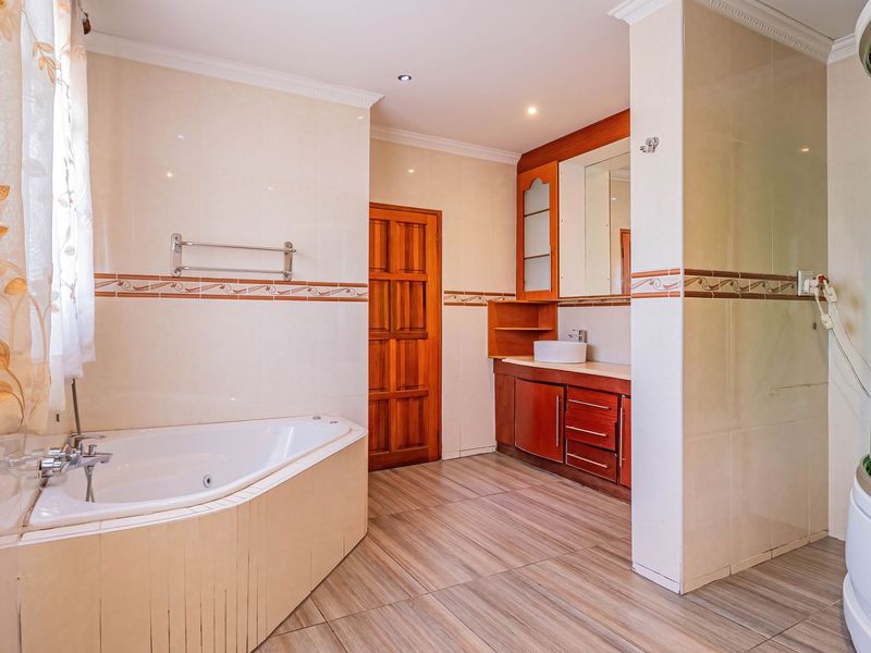 Spacious bathroom featuring a corner bathtub, separate enclosed shower cubicle, wooden vanity with vessel sink, and neutral wall tiling.