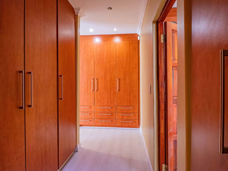 A well-maintained hallway featuring extensive built-in wooden cabinetry, recessed lighting, and light-toned laminate flooring.