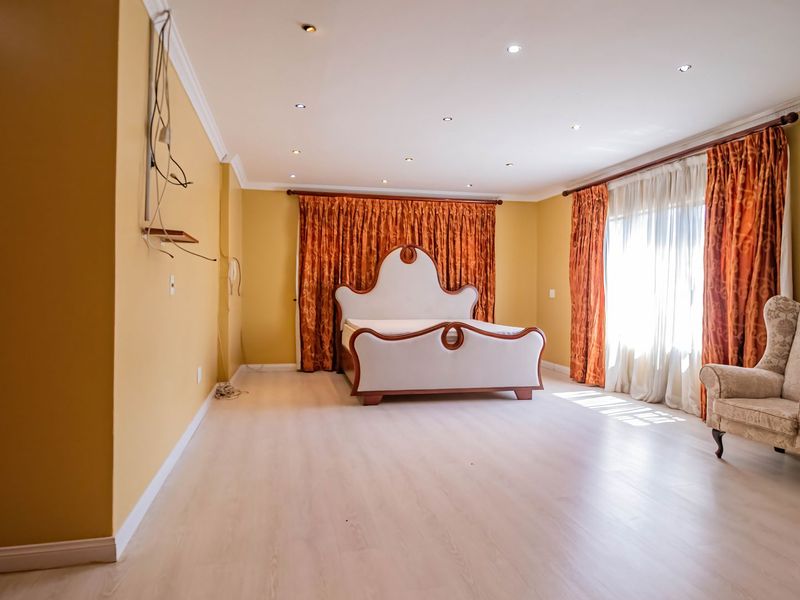 Spacious bedroom featuring light-toned laminate flooring, recessed ceiling lighting, and crown molding, with exposed wall wiring requiring attention.