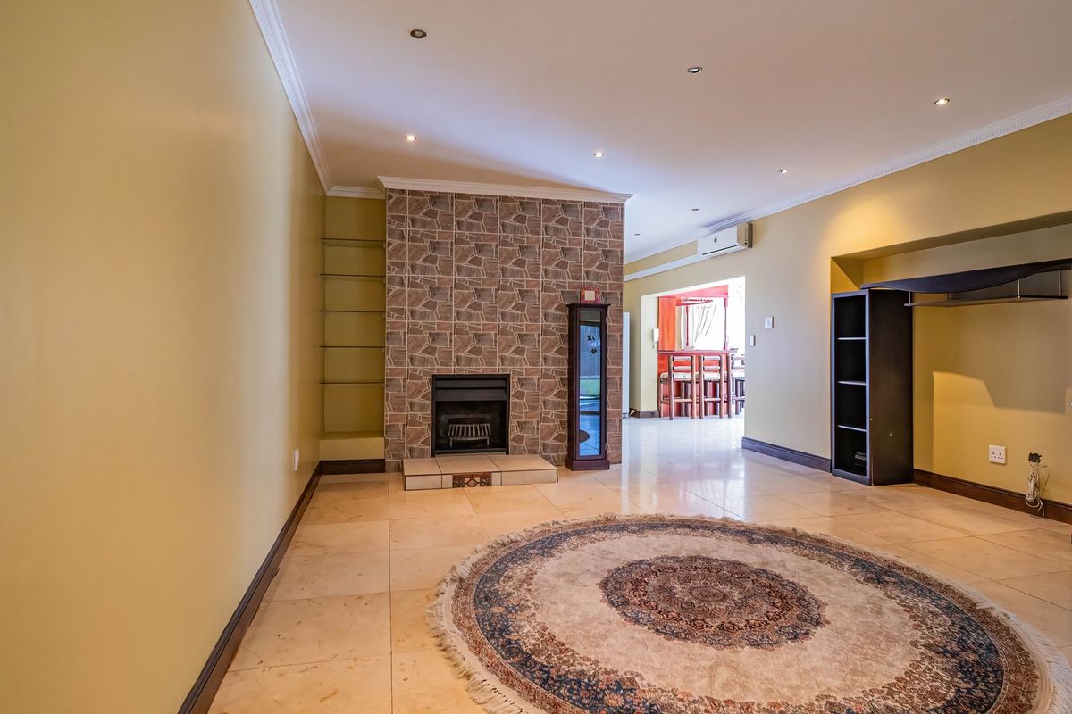 Spacious living area featuring a prominent stone-clad fireplace, tiled flooring, recessed lighting, and an integrated air conditioning unit, leading into an adjacent dining space.