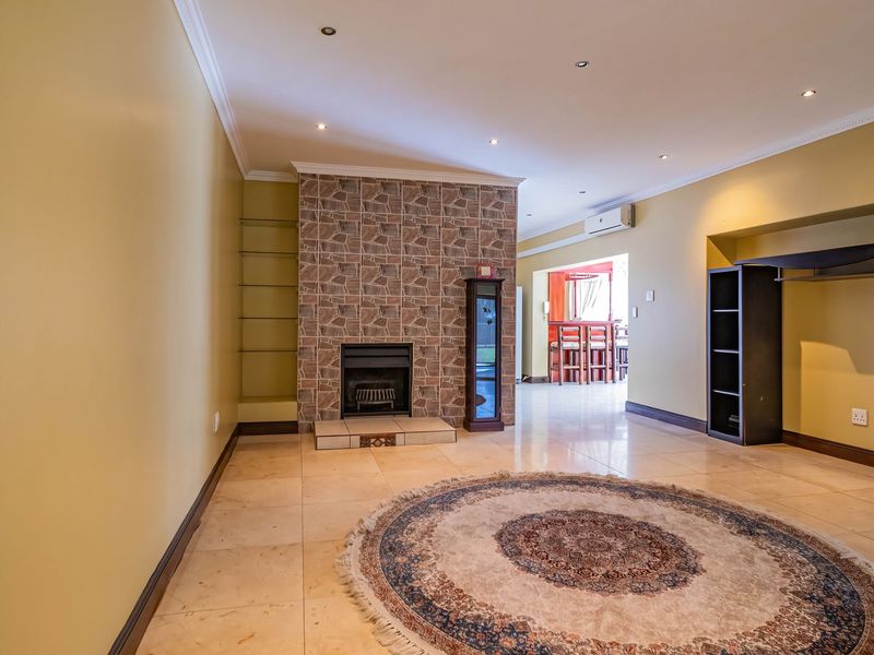Spacious living area featuring a prominent stone-clad fireplace, tiled flooring, recessed lighting, and an integrated air conditioning unit, leading into an adjacent dining space.