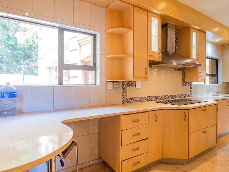 A spacious kitchen featuring light wood cabinetry, stone countertops, a built-in electric hob with extractor fan, and tiled flooring throughout.