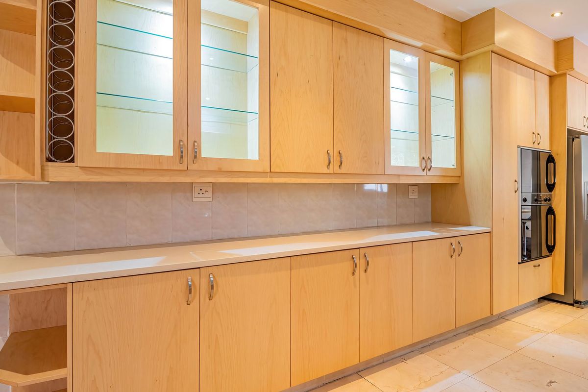 A well-maintained kitchen featuring light wood cabinetry, glass display units, stone countertops, and a built-in double oven with integrated stainless steel appliances.
