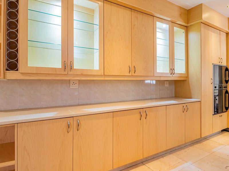 A well-maintained kitchen featuring light wood cabinetry, glass display units, stone countertops, and a built-in double oven with integrated stainless steel appliances.