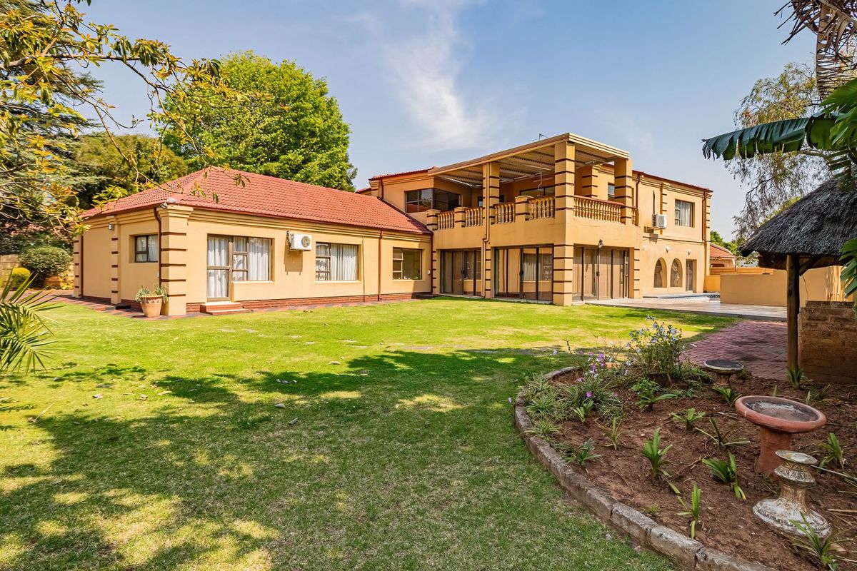 Spacious rear exterior view of the house featuring a large lawn, a covered balcony, and a traditional thatched lapa area.