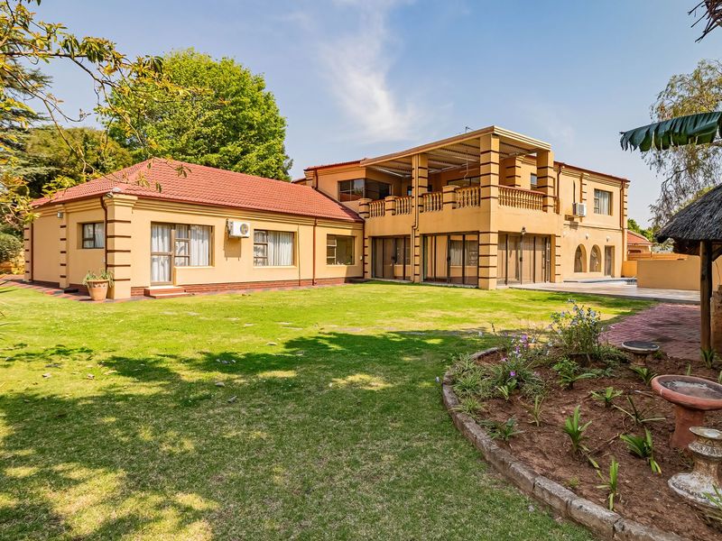 Spacious rear exterior view of the house featuring a large lawn, a covered balcony, and a traditional thatched lapa area.
