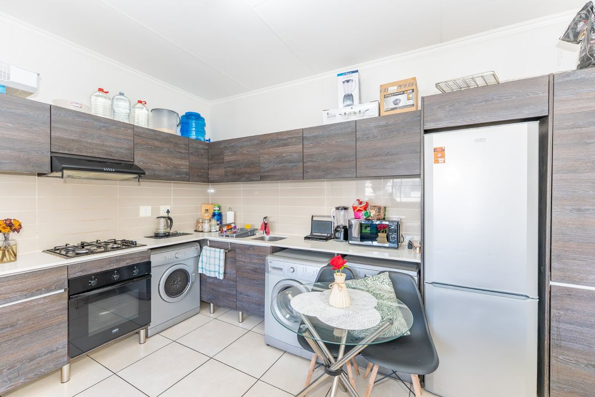 A functional kitchen featuring modern wood-grain cabinetry, a gas hob with extractor, electric oven, and integrated space for laundry appliances.