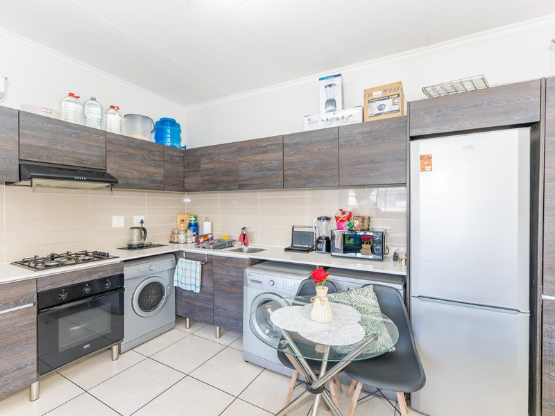 A functional kitchen featuring modern wood-grain cabinetry, a gas hob with extractor, electric oven, and integrated space for laundry appliances.