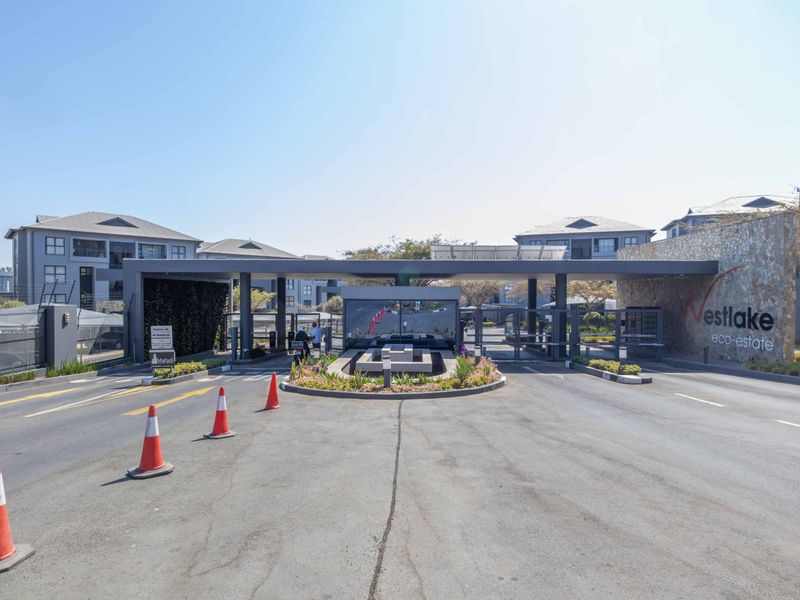 The main entrance and security gatehouse of Westlake Eco-Estate, featuring modern stone cladding, controlled access boom gates, and a landscaped traffic island.