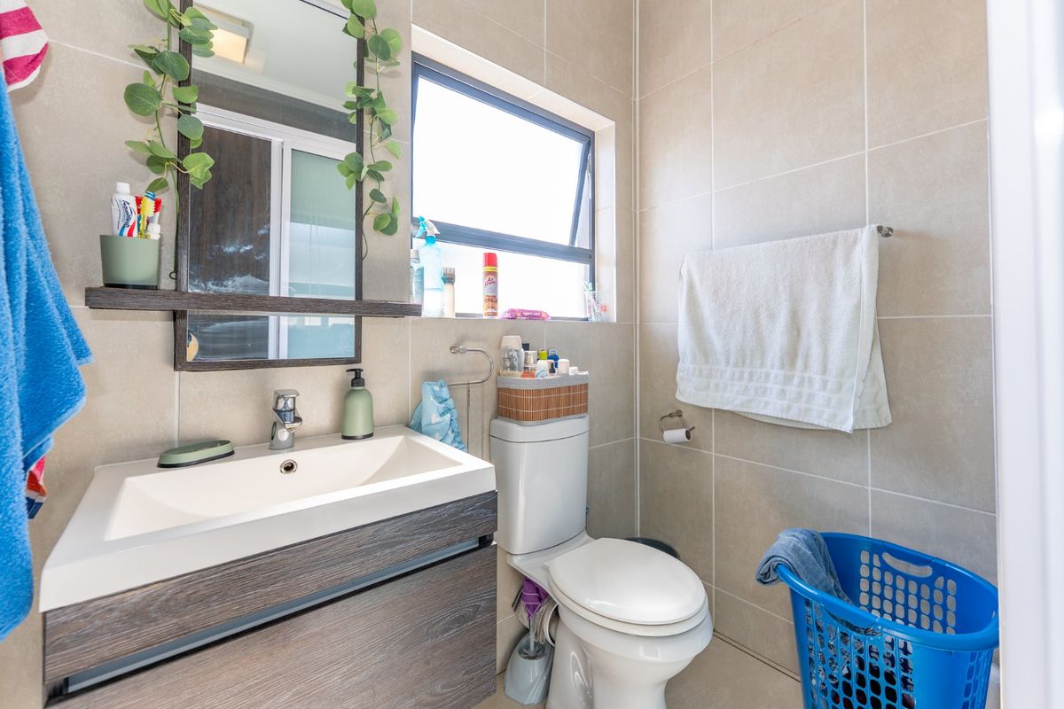 A compact, modern bathroom featuring a vanity cabinet with a basin, a wall-mounted mirror, a toilet, and neutral wall tiling.