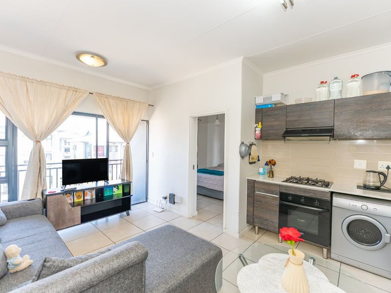 Open-plan living area featuring a compact kitchen with built-in cabinetry, gas hob, oven, and tiled flooring, with direct access to a balcony.