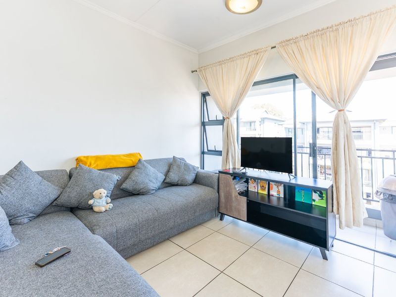 A bright living room featuring tiled flooring and a large sliding glass door that provides access to an outdoor balcony area.